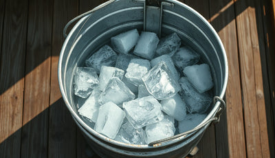 Galvanized metal ice bath tub filled with water and large ice chunks on a wooden deck